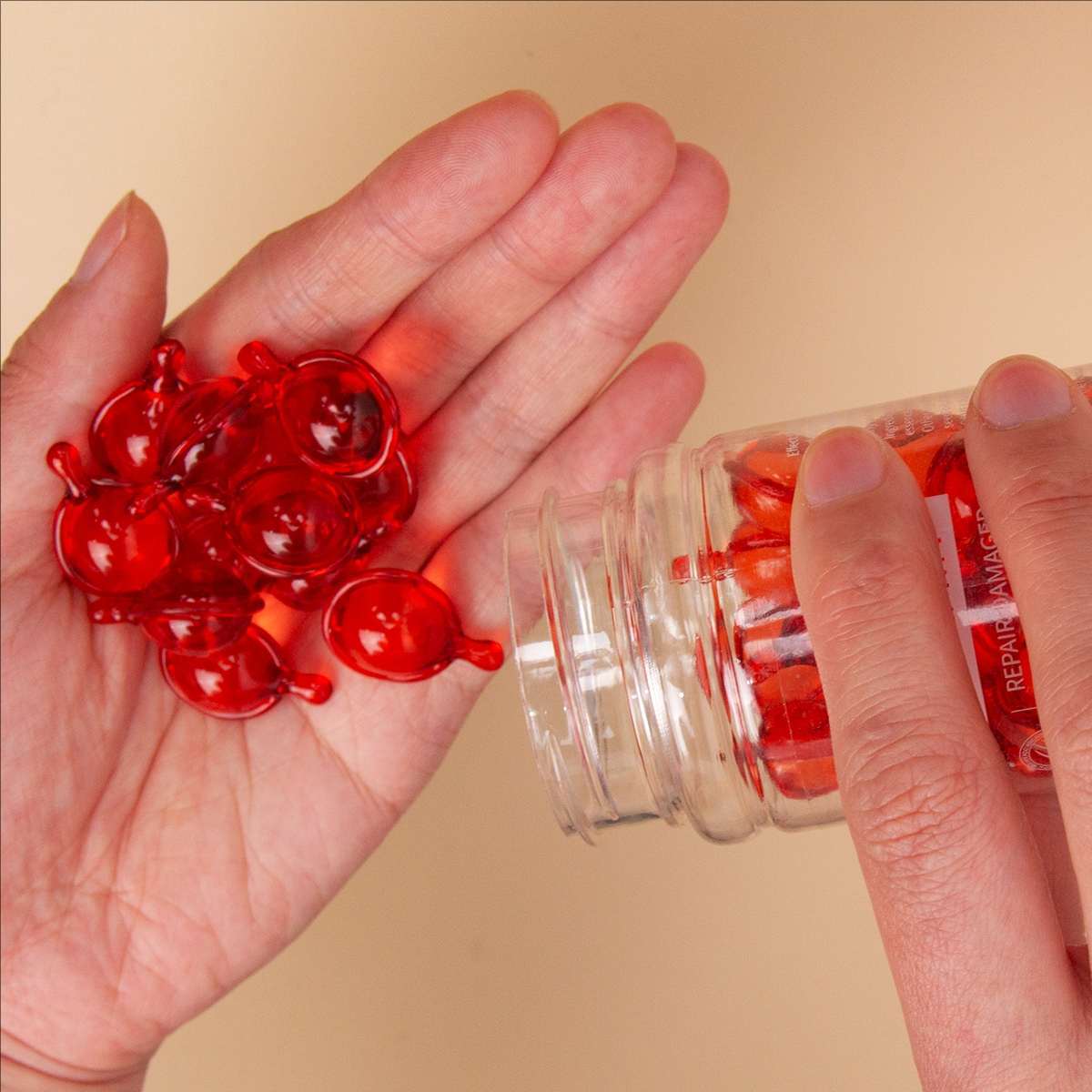 Hands holding a jar of glossy red hair treatment capsules, featuring an assortment of moisturizing oils like Argan, Macadamia, and Avocado, for a nourishing and non-rinse formula.